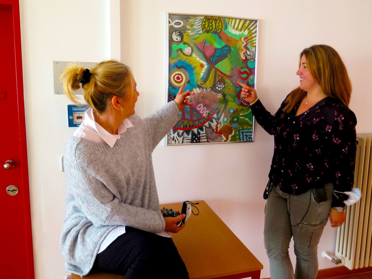 Sozialpädagoginnen Andrea Koch und Johanna Tesch vor einem gemalten Bild eines Inhaftierten 